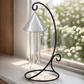 Indoor solar wind chime with a pewter colored top and hanging tubes, mounted on a black wrought-iron scrollwork stand, set on a windowsill in front of a sunny window