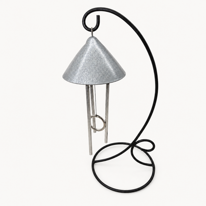 An indoor pewter colored solar wind chime featuring a textured silver metal cone-shaped top and three silver hanging rods, supported by a curved black metal stand